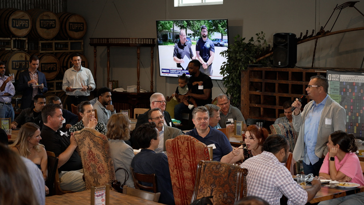 Builders seated around long tables, listening to an intro